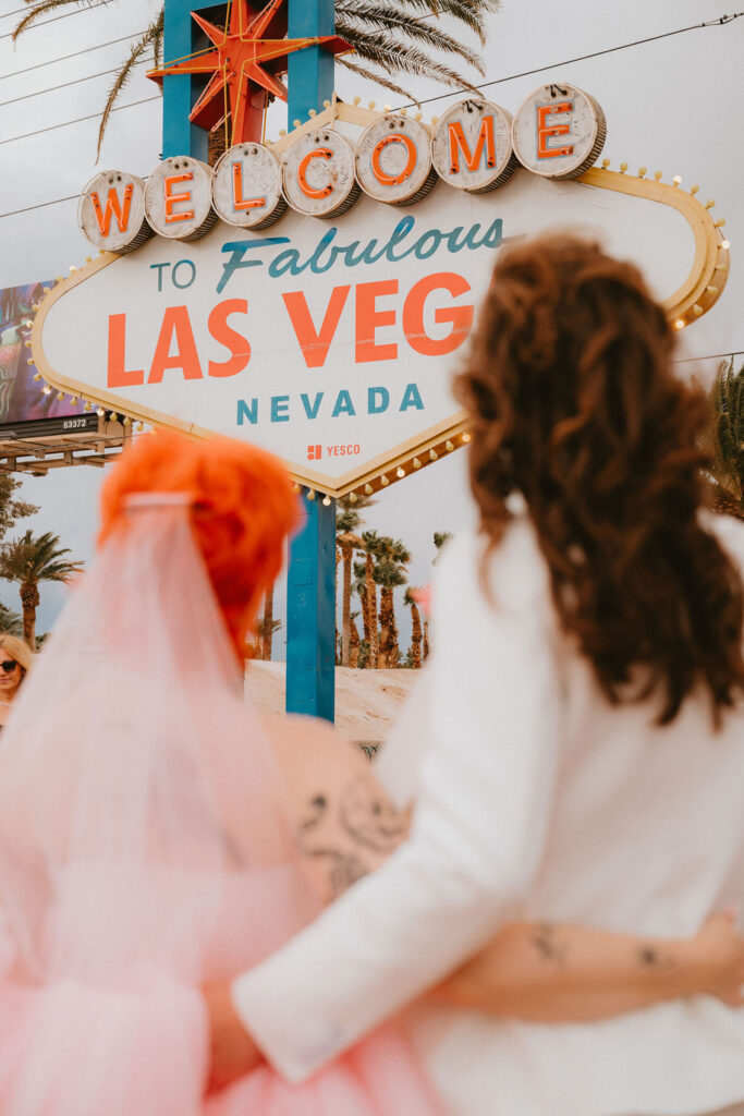 Stylish wedding portraits at the Welcome to Las Vegas sign with the couple laughing together.
