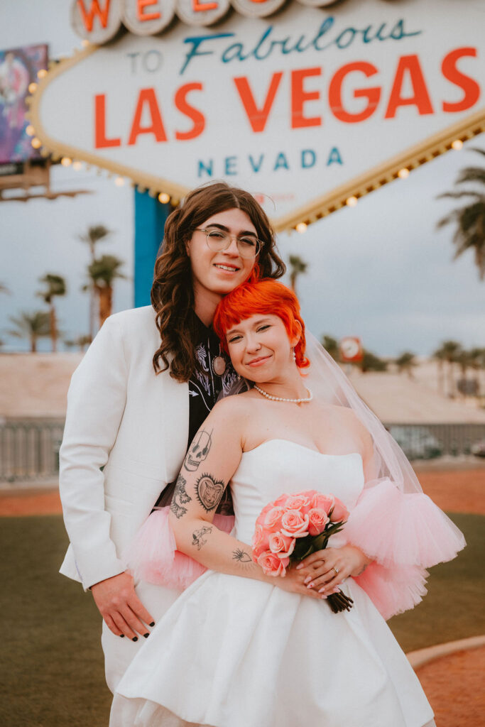 Stylish wedding portraits at the Welcome to Las Vegas sign with the couple laughing together.
