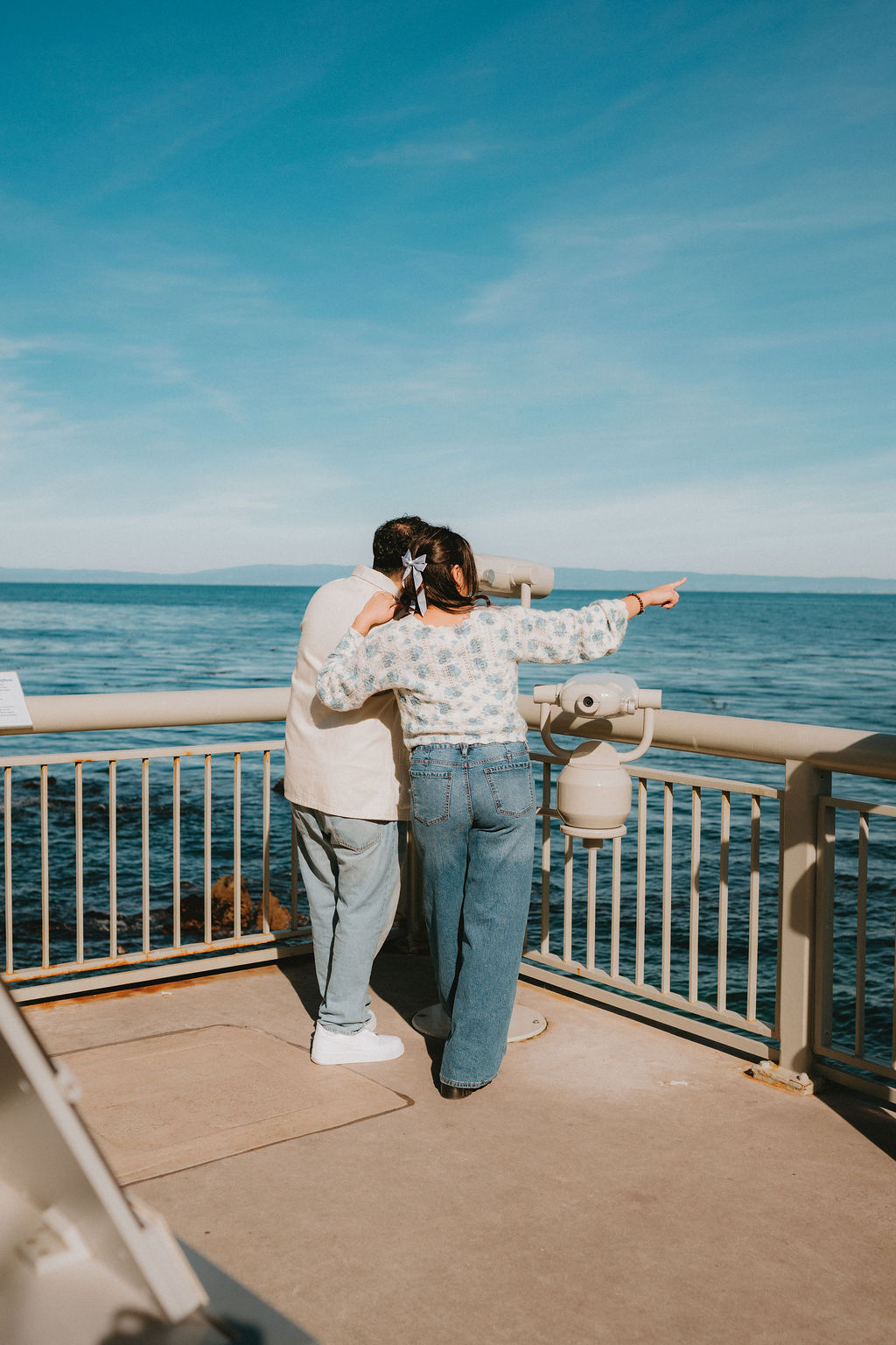 Couple points out into ocean at their Monterey Bay Aquarium engagement photoshoot